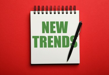Image of New Trends inscription in notebook and pen on red background, top view