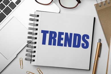 Image of Trends inscription in notebook, laptop and stationery on white table, top view