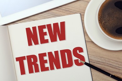 Image of New Trends inscription in notebook, coffee and pen on wooden table, top view