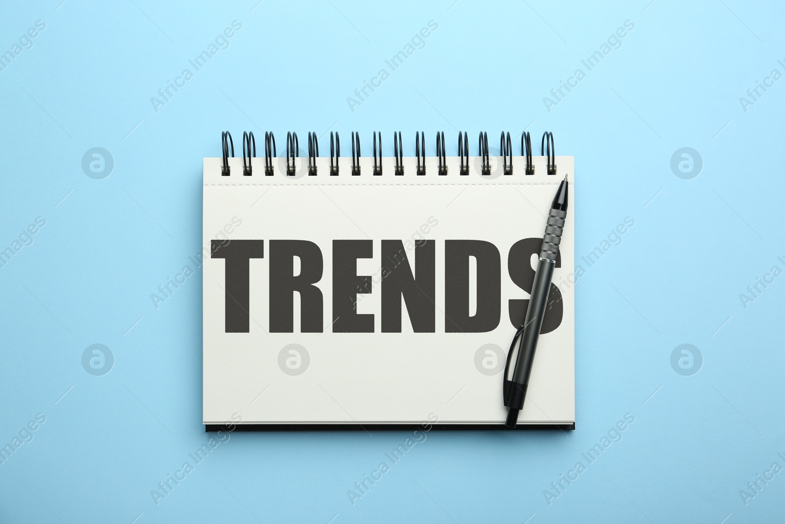 Image of Trends inscription in notebook and pen on light blue background, top view