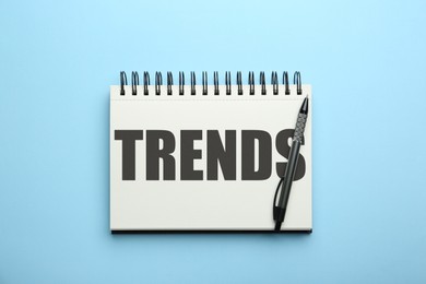 Image of Trends inscription in notebook and pen on light blue background, top view