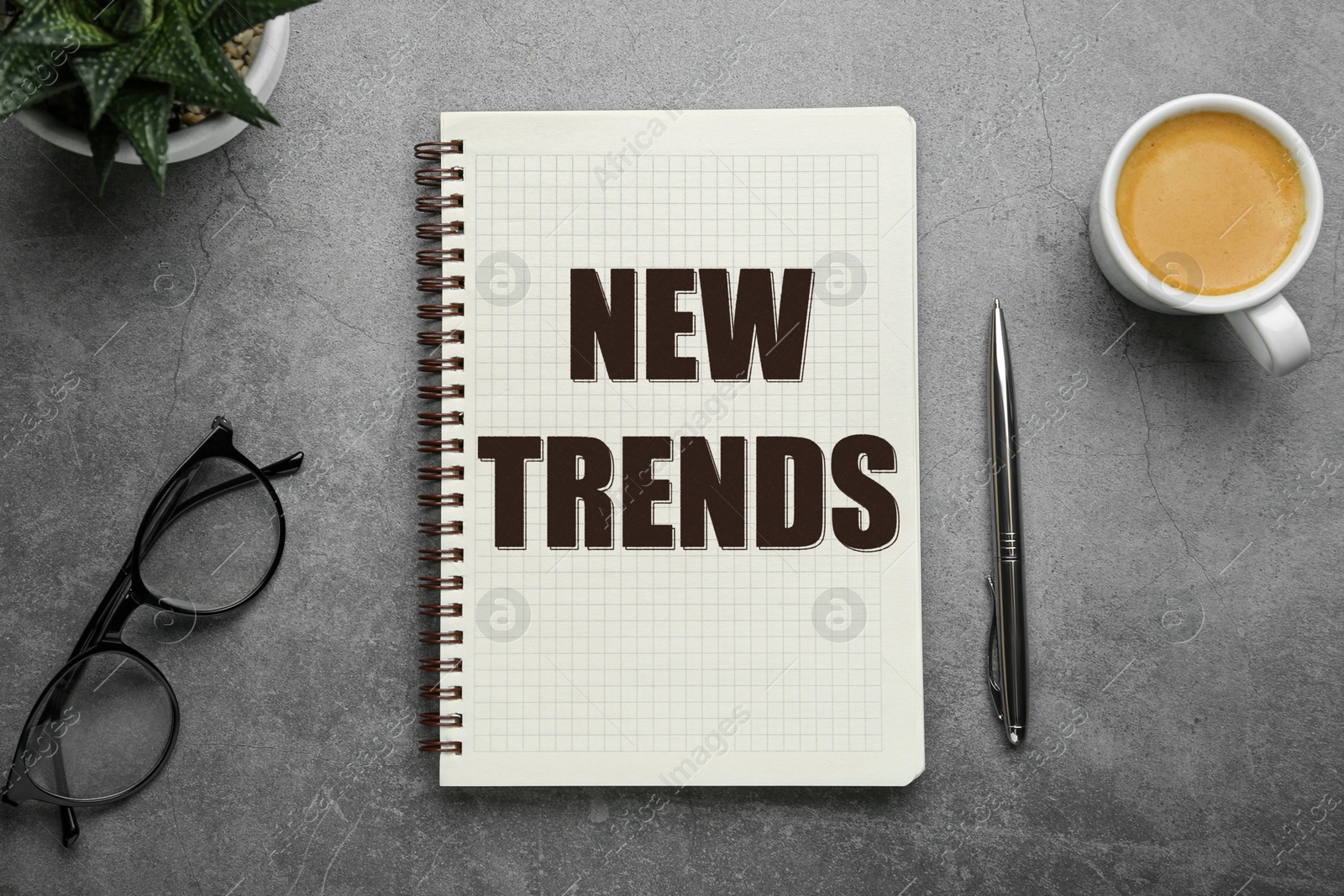 New Trends inscription in notebook, coffee, glasses and pen on grey table, top view Image of New Trends inscription in notebook, coffee, glasses and pen on grey table, top view