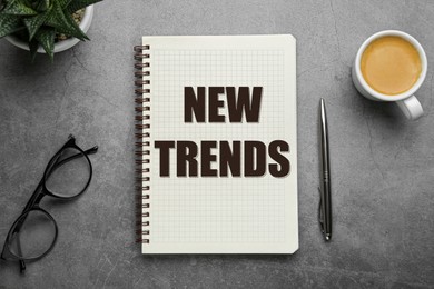 Image of New Trends inscription in notebook, coffee, glasses and pen on grey table, top view
