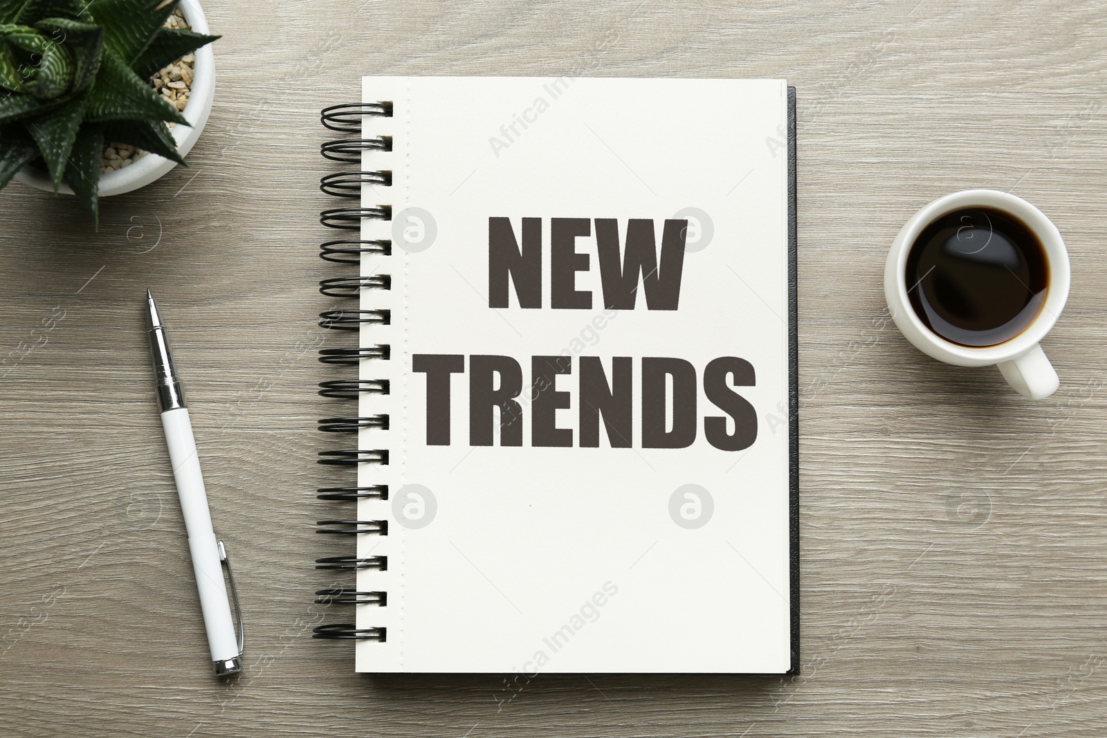New Trends inscription in notebook, coffee and pen on wooden table, top view Image of New Trends inscription in notebook, coffee and pen on wooden table, top view