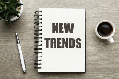 Image of New Trends inscription in notebook, coffee and pen on wooden table, top view