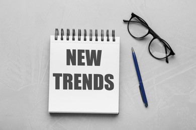 Image of New Trends inscription in notebook, glasses and pen on red background, top view