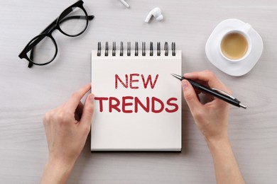 Image of New trends. Woman with notebook and pen at white wooden table, top view