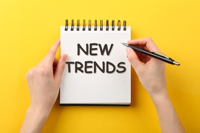 Image of New trends. Woman with notebook and pen on yellow background, top view