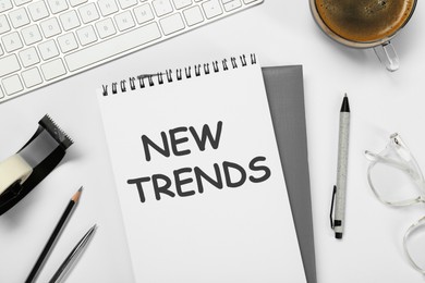 Image of New Trends inscription in notebook, coffee, computer keyboard and stationery on white table, top view