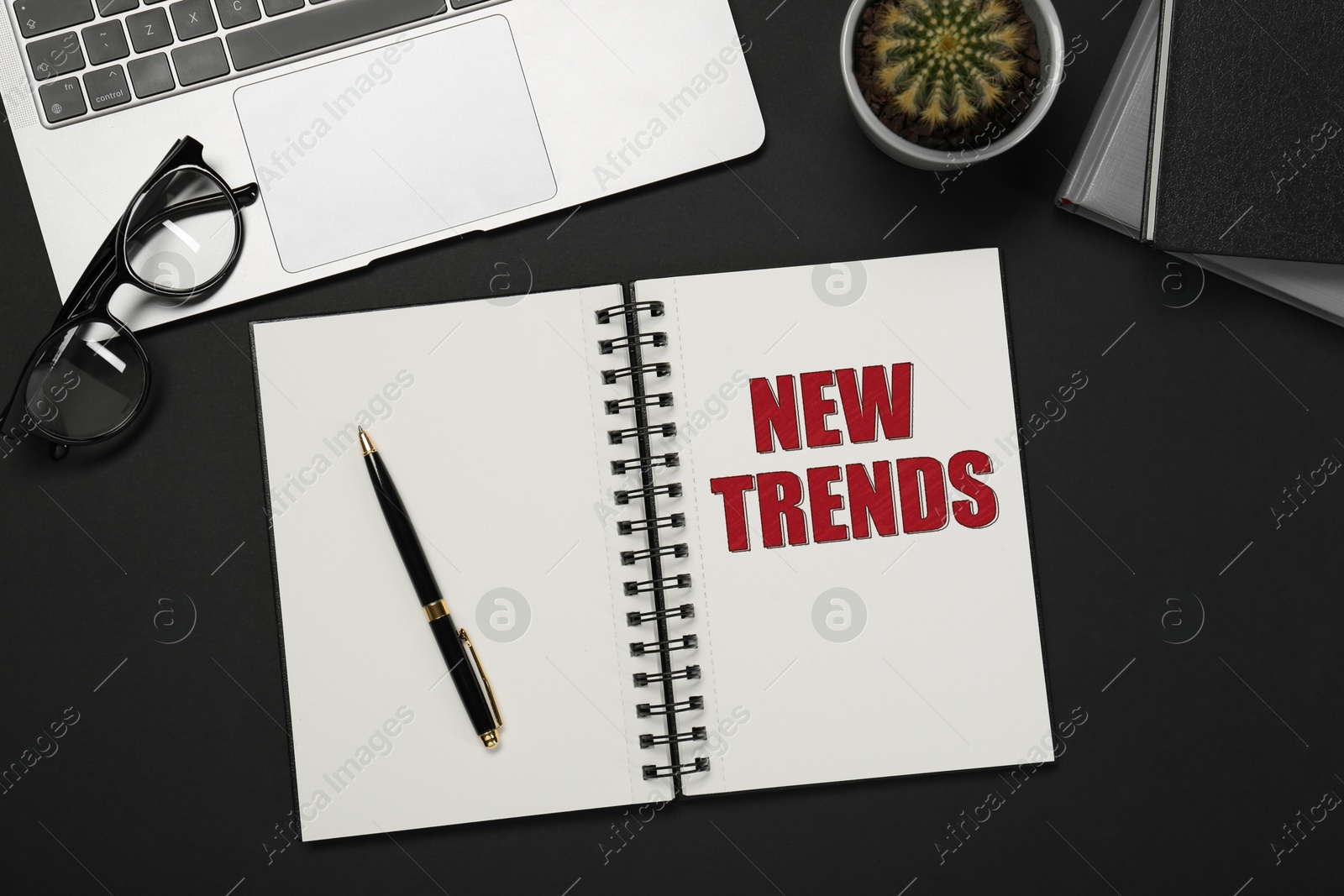 New Trends inscription in notebook, laptop, glasses and pen on black table, top view Image of New Trends inscription in notebook, laptop, glasses and pen on black table, top view