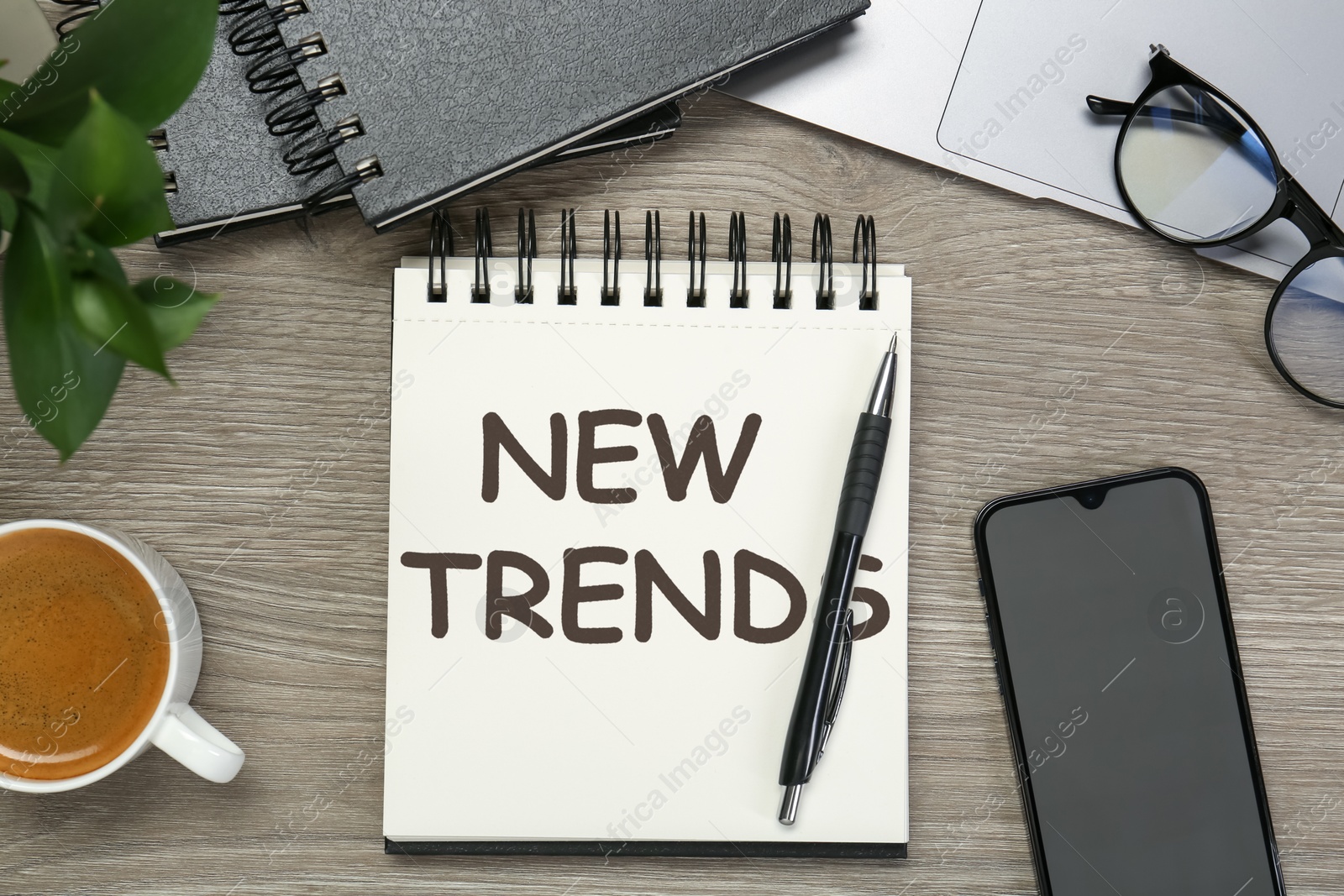 New Trends inscription in notebook, coffee, laptop, smartphone and pen on wooden table, top view Image of New Trends inscription in notebook, coffee, laptop, smartphone and pen on wooden table, top view