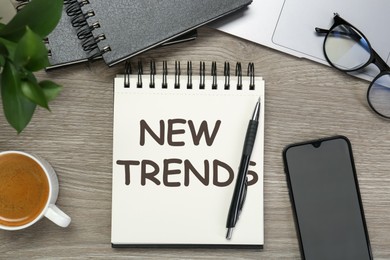 Image of New Trends inscription in notebook, coffee, laptop, smartphone and pen on wooden table, top view