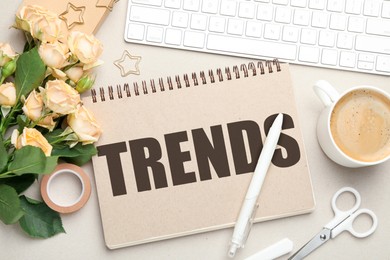 Image of Trends inscription in notebook, flowers, computer keyboard, coffee and stationery on beige table, top view