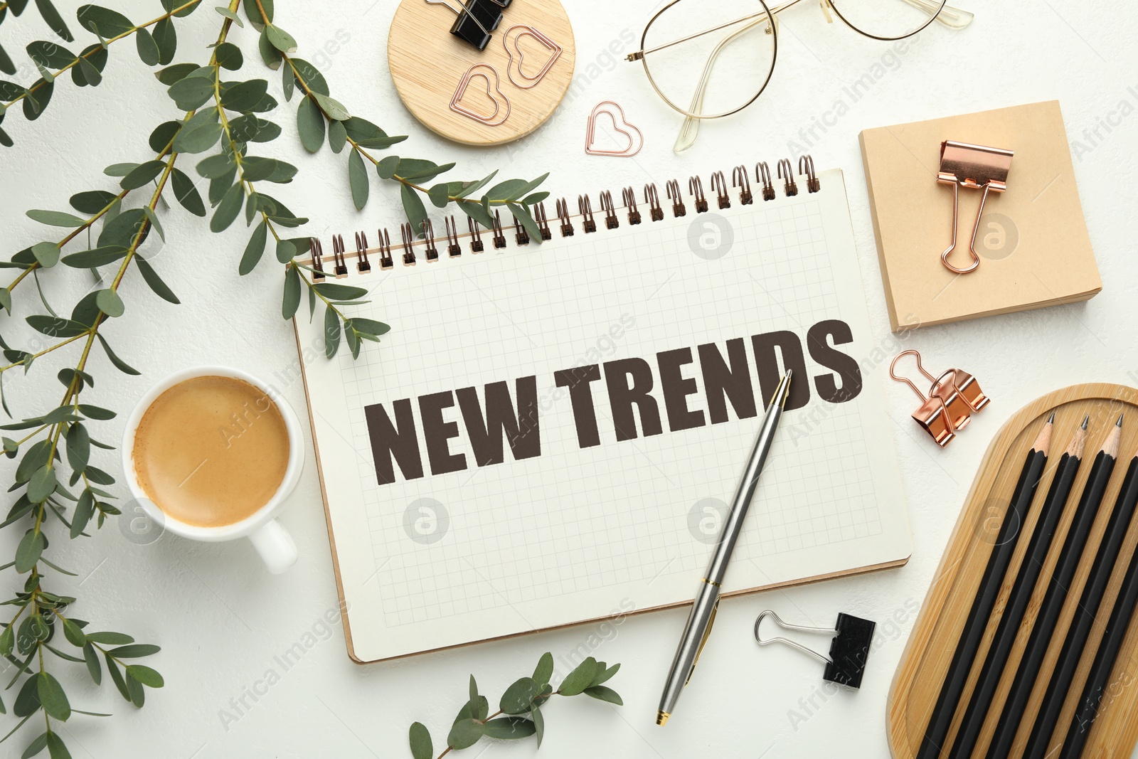 Image of New Trends inscription in notebook, coffee and stationery on white table, top view