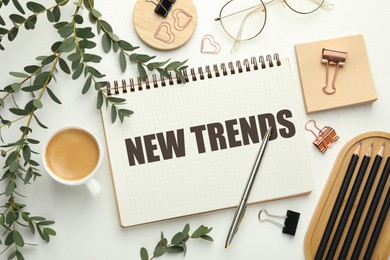 Image of New Trends inscription in notebook, coffee and stationery on white table, top view