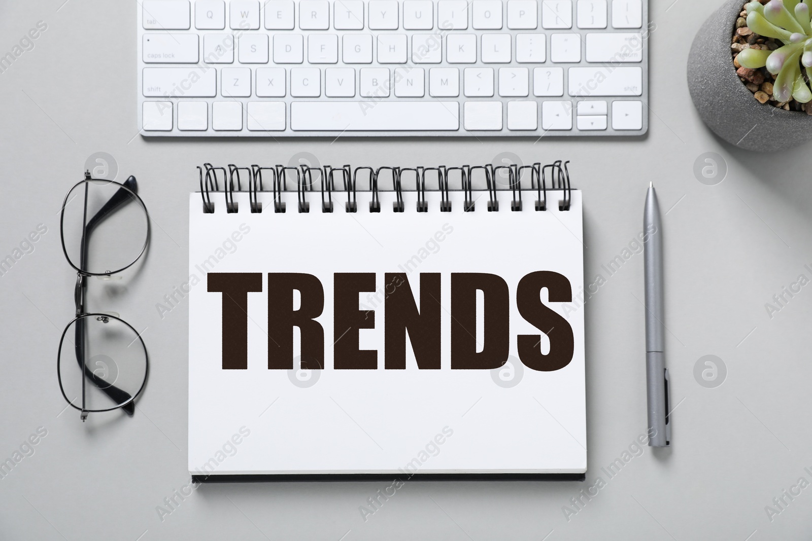 Image of Trends inscription in notebook, computer keyboard, glasses and pen on white table, top view