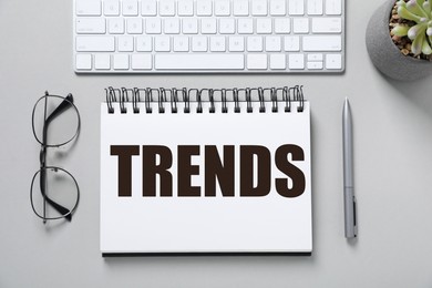 Image of Trends inscription in notebook, computer keyboard, glasses and pen on white table, top view