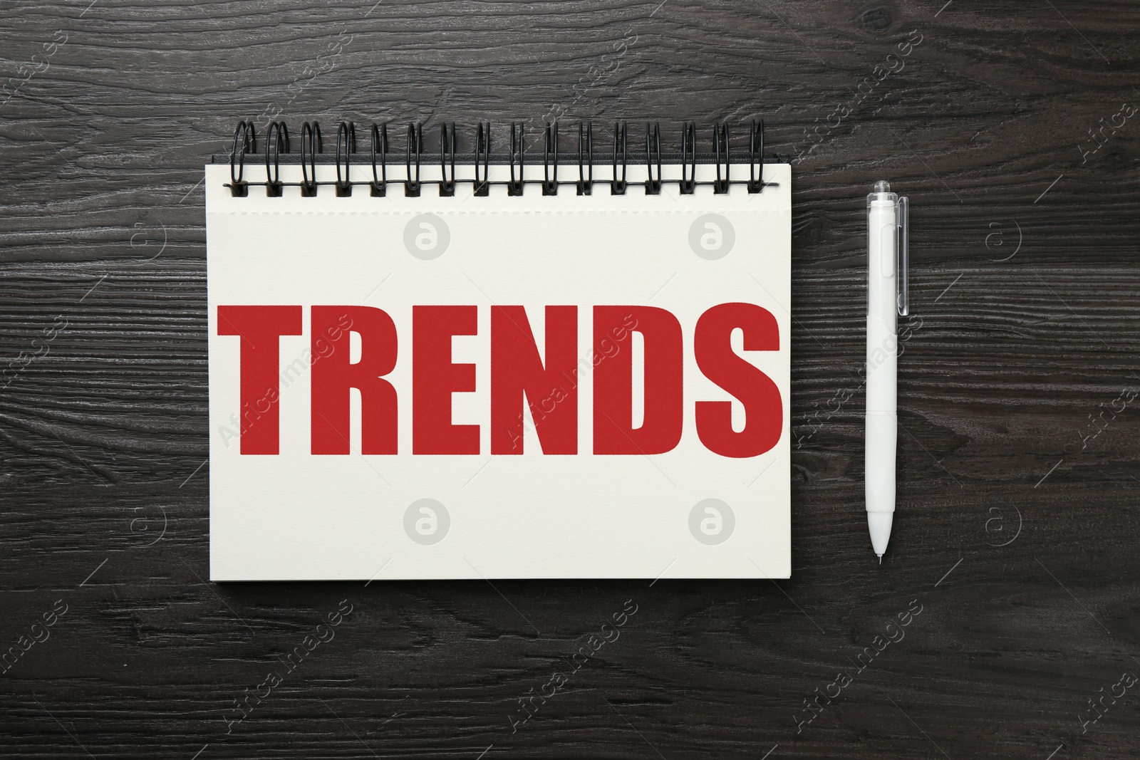 Image of Trends inscription in notebook and pen on wooden table, top view
