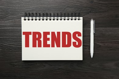 Image of Trends inscription in notebook and pen on wooden table, top view