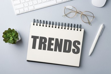 Image of Trends inscription in notebook, computer keyboard, glasses and pen on white table, top view