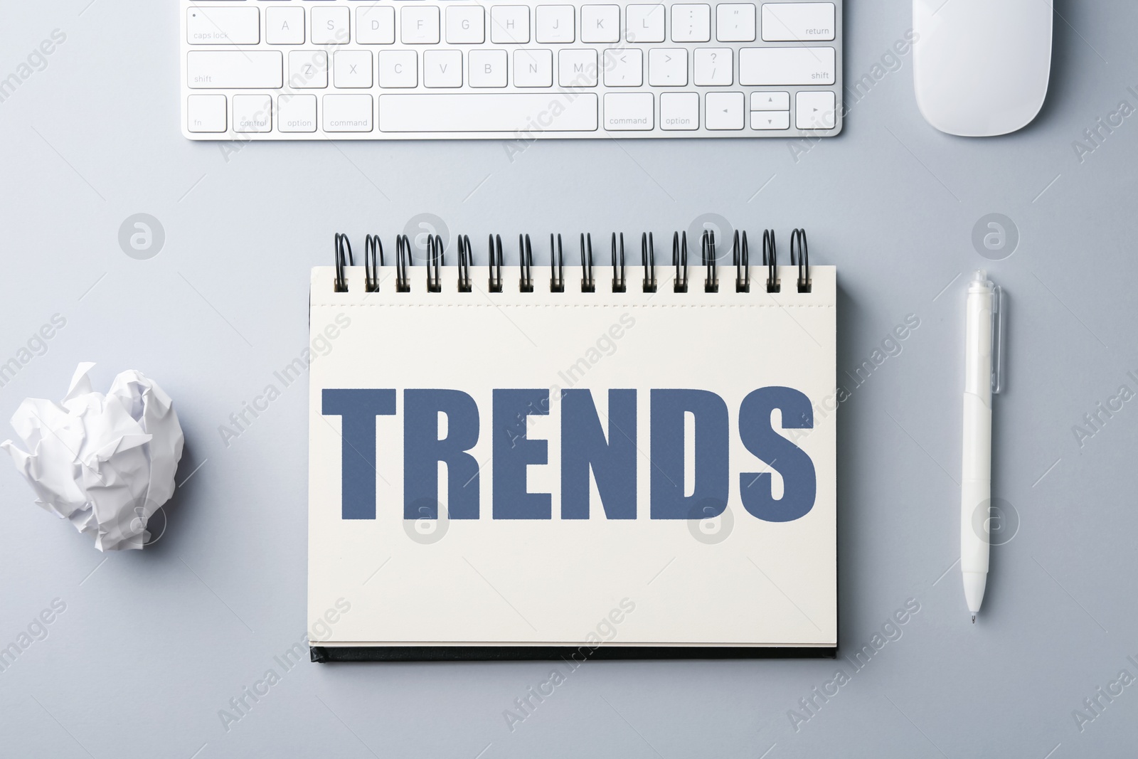Image of Trends inscription in notebook, computer keyboard, mouse, crumpled paper ball and pen on white table, top view