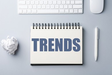 Image of Trends inscription in notebook, computer keyboard, mouse, crumpled paper ball and pen on white table, top view