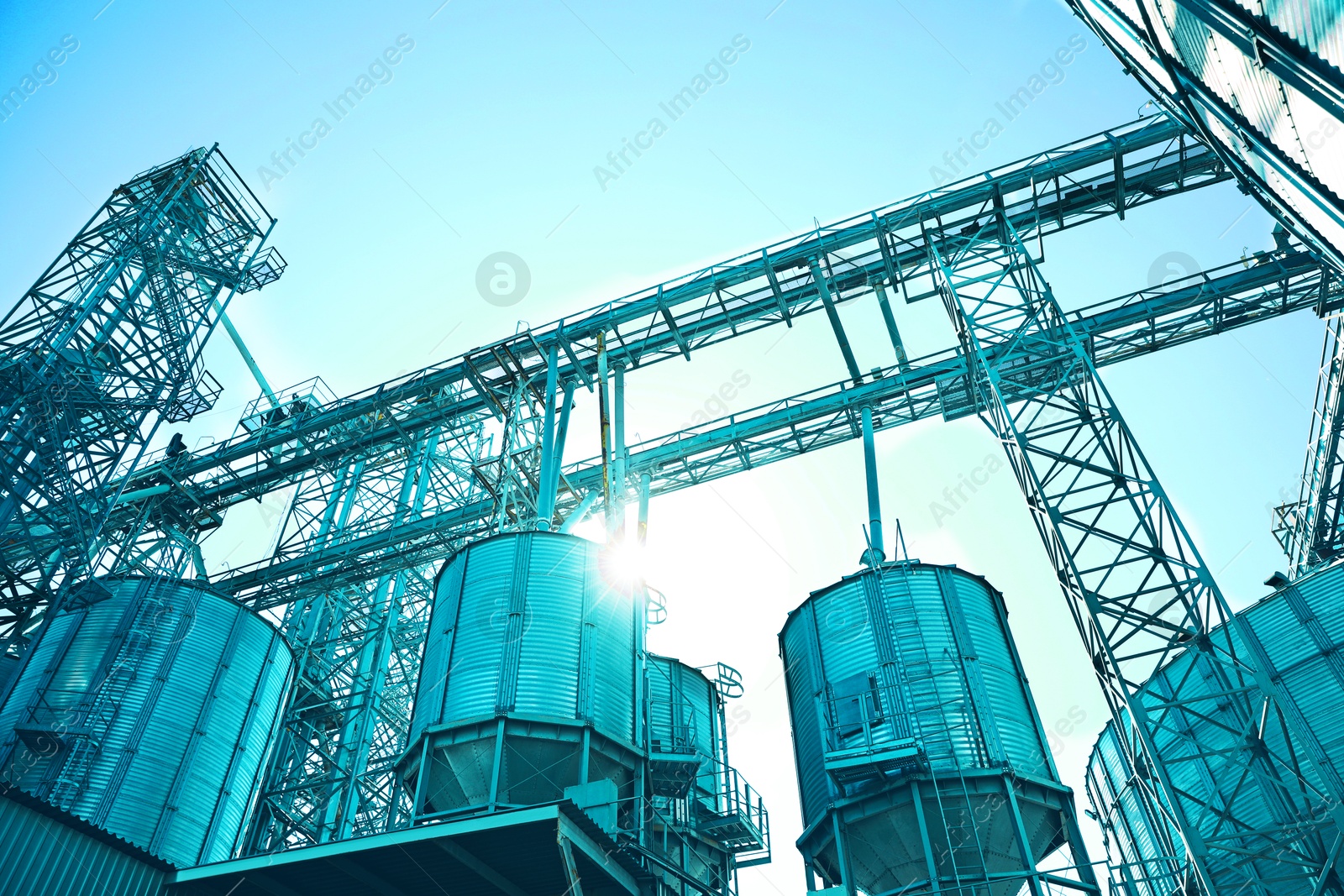 Modern granaries for storing cereal grains against sky, low angle view. Toned in light blue Image of Modern granaries for storing cereal grains against sky, low angle view. Toned in light blue