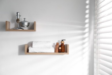 Photo of Wooden shelves with bathroom necessities on white wall