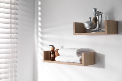 Photo of Wooden shelves with bathroom necessities on white wall
