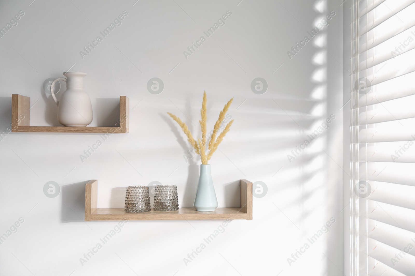 Wooden shelves with tableware and spikes in vase on white wall Photo of Wooden shelves with tableware and spikes in vase on white wall