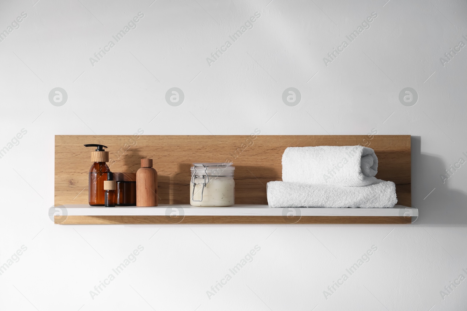 Wooden shelf with cosmetic products and towels on white background Photo of Wooden shelf with cosmetic products and towels on white background