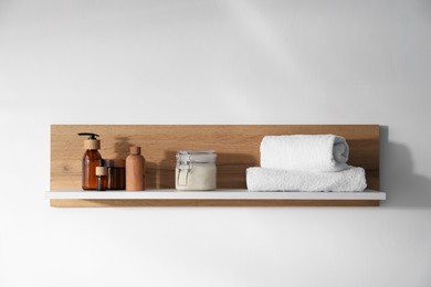 Photo of Wooden shelf with cosmetic products and towels on white background
