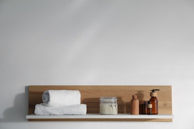 Photo of Wooden shelf with cosmetic products and towels on white background. Space for text