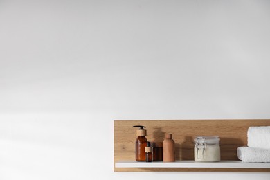 Photo of Wooden shelf with cosmetic products and towels on white background. Space for text