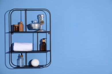 Photo of Metal shelving unit with towel and cosmetic products on blue background. Space for text