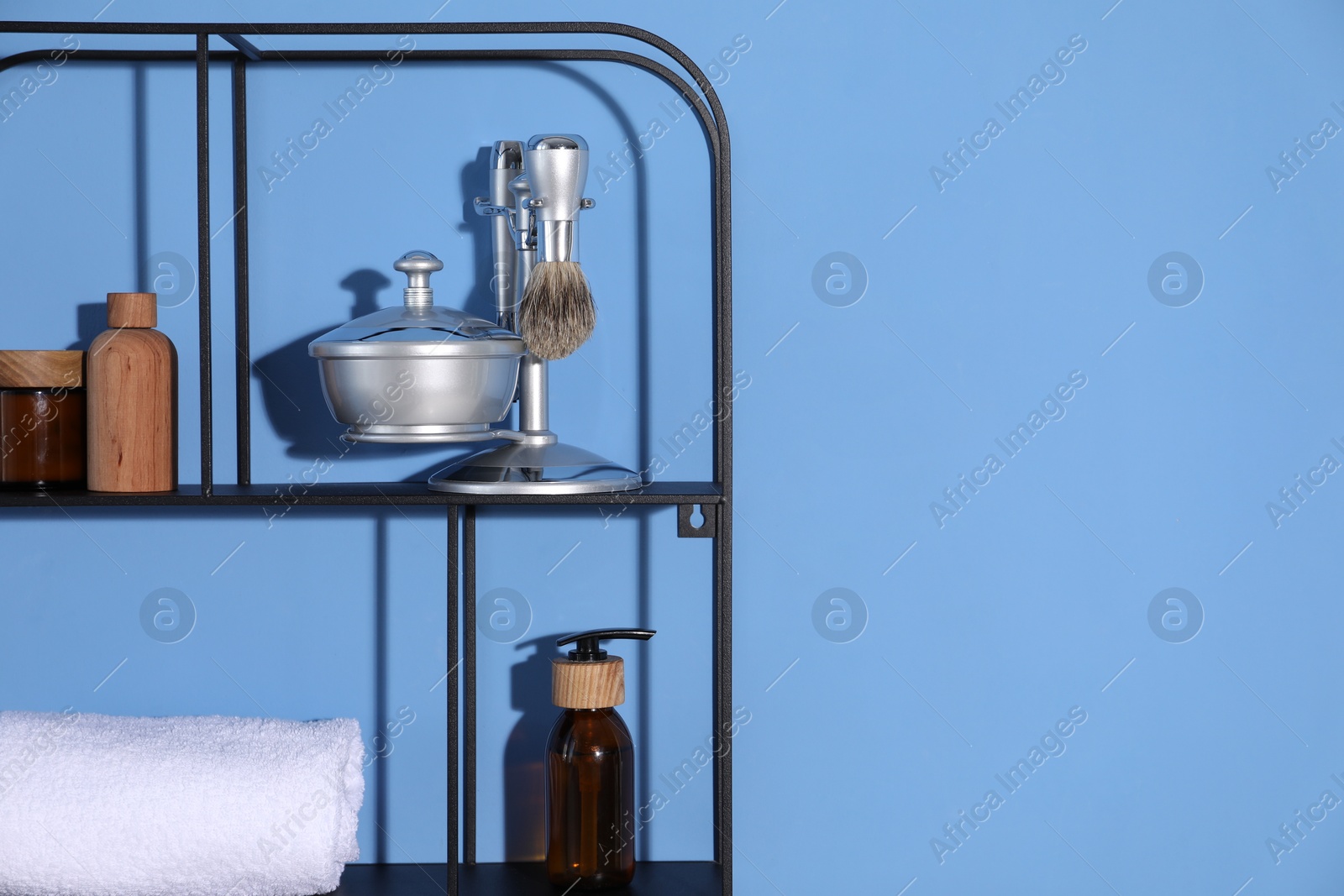 Metal shelving unit with towel and cosmetic products on blue background. Space for text Photo of Metal shelving unit with towel and cosmetic products on blue background. Space for text