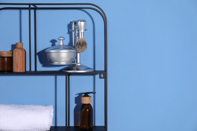Photo of Metal shelving unit with towel and cosmetic products on blue background. Space for text