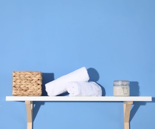 Photo of Shelf with towels, cosmetic product and basket on blue background. Space for text