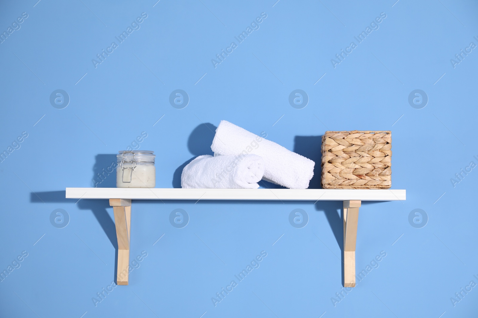 Photo of Shelf with towels, cosmetic product and basket on blue background