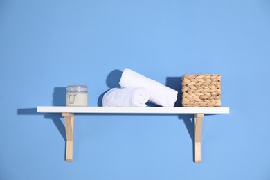 Photo of Shelf with towels, cosmetic product and basket on blue background