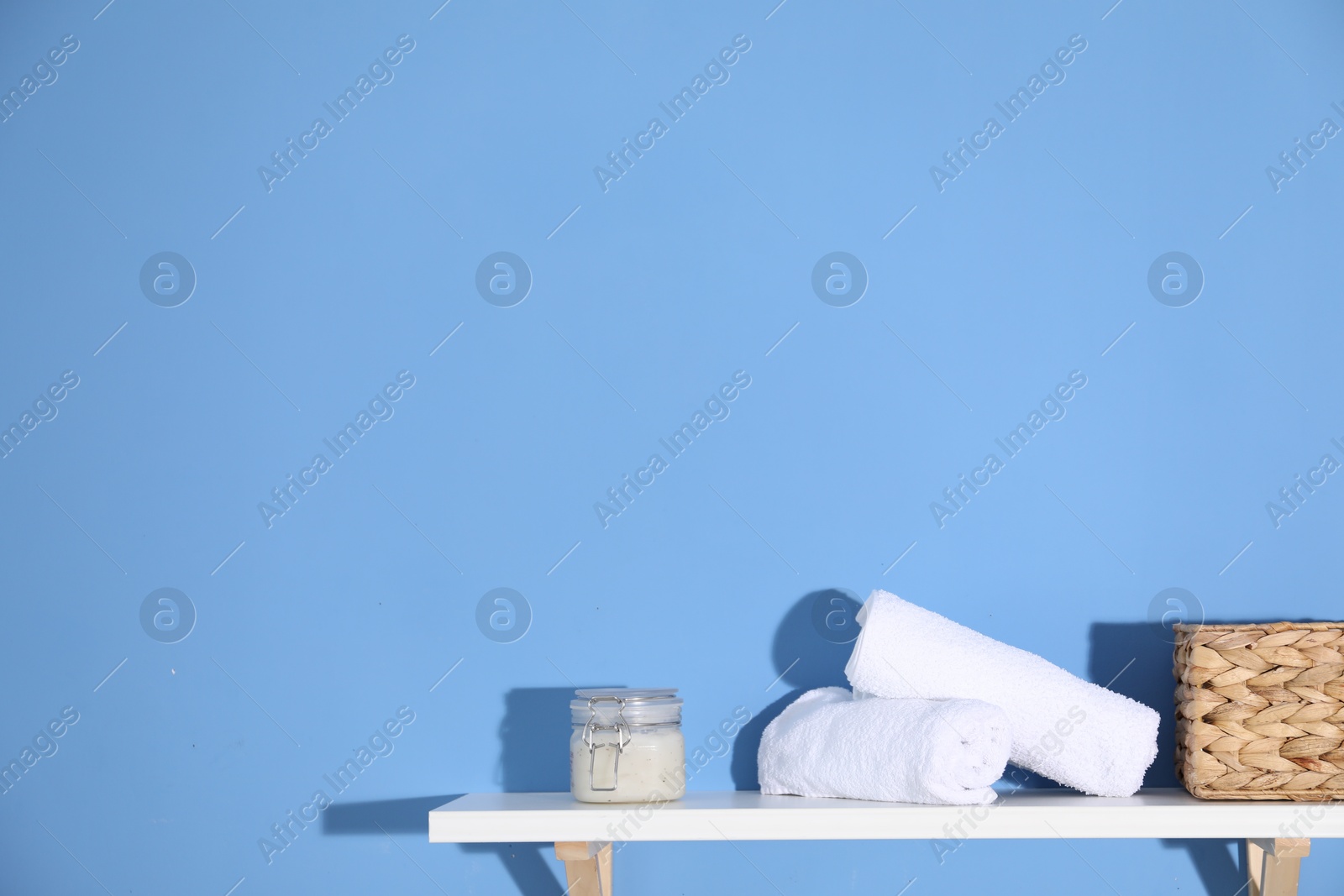Photo of Shelf with towels, cosmetic product and basket on blue background. Space for text