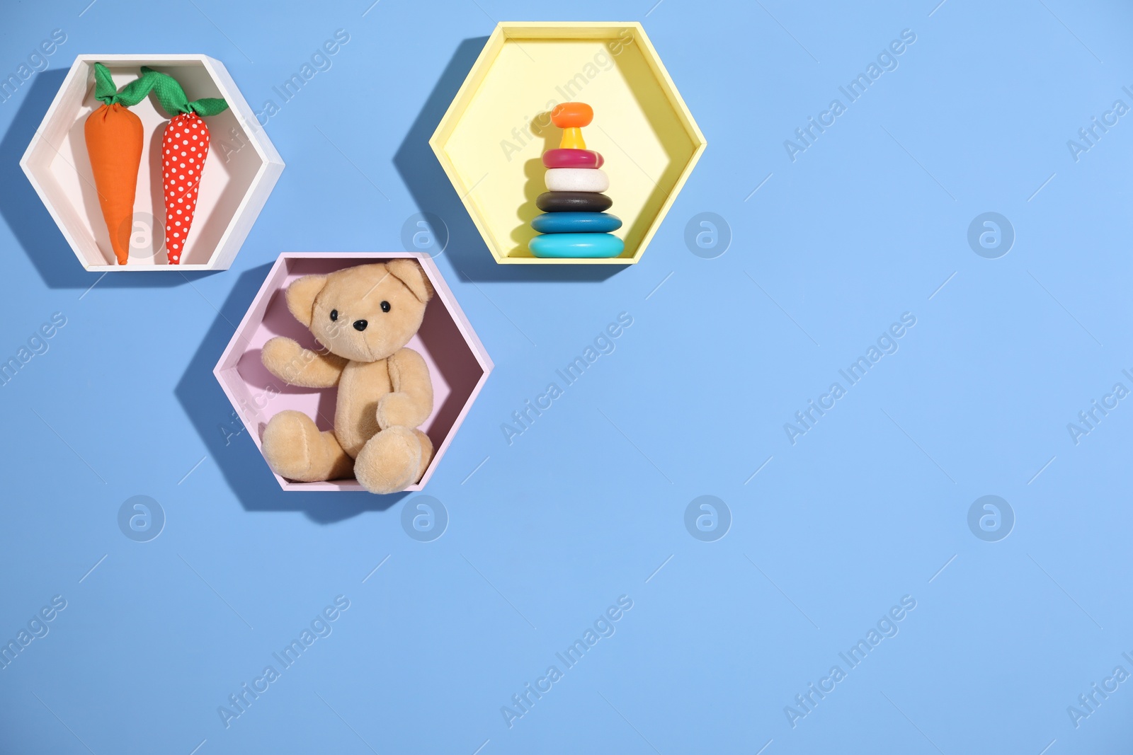 Photo of Honeycomb shaped shelves with different toys on blue background. Space for text