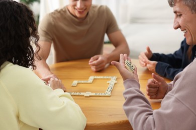 Photo of Friends playing dominoes at wooden table indoors, closeup