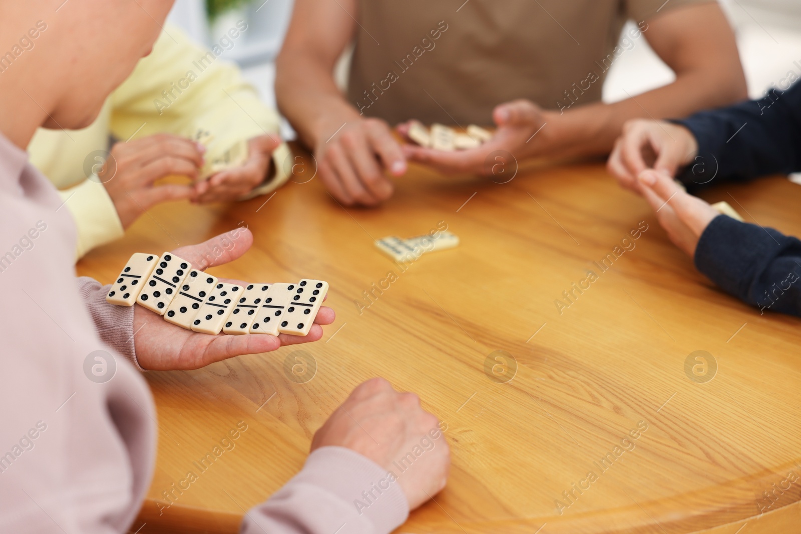 Friends playing dominoes at wooden table, closeup Photo of Friends playing dominoes at wooden table, closeup