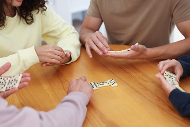Photo of Friends playing dominoes at wooden table, closeup