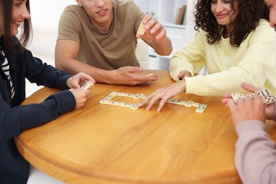 Photo of Friends playing dominoes at wooden table indoors, closeup