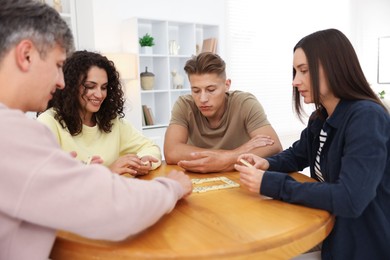 Photo of Friends playing dominoes at wooden table indoors