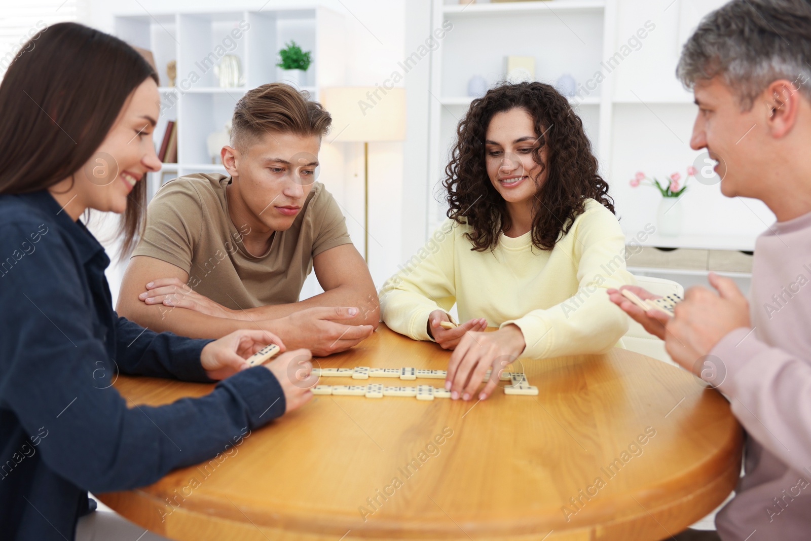 Friends playing dominoes at wooden table indoors Photo of Friends playing dominoes at wooden table indoors