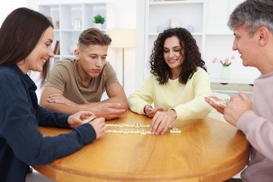 Photo of Friends playing dominoes at wooden table indoors