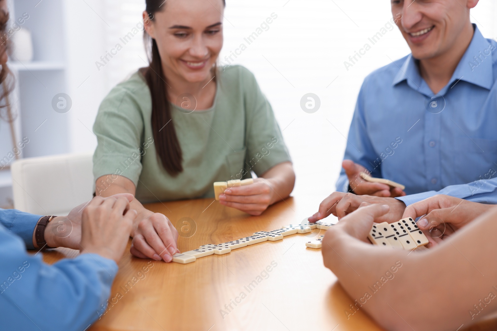 Happy friends playing dominoes at wooden table indoors, closeup Photo of Happy friends playing dominoes at wooden table indoors, closeup